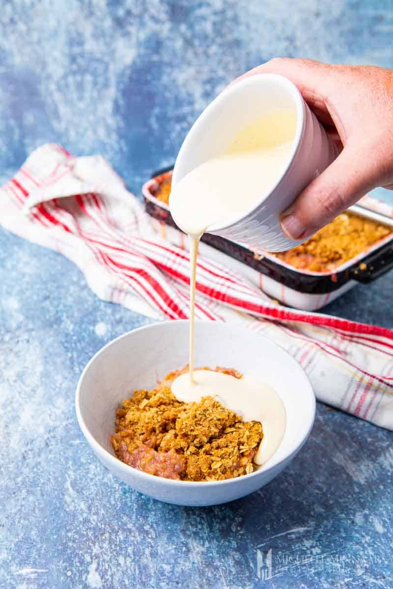 Cream being poured into a bowl of apple and rhubarb crumble