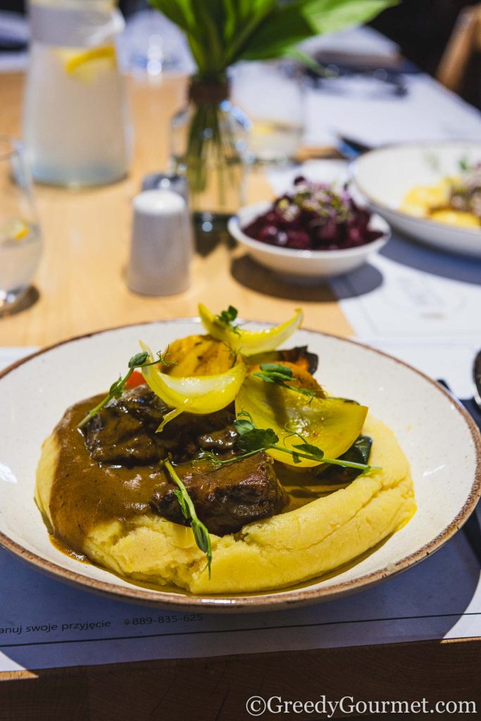 Beef cheeks and mash on a plate with vegetables.