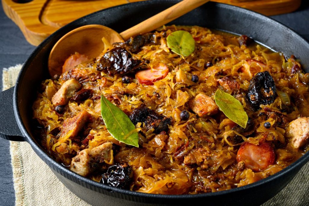 Serving of Bigos in a black bowl with a wooden spoon.