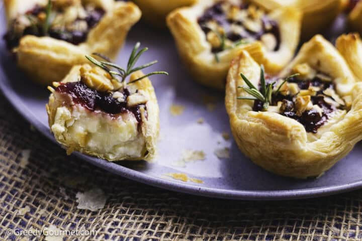 pastry filled with cheese and jam bitten through and on blue plate along with other intact pastry cups