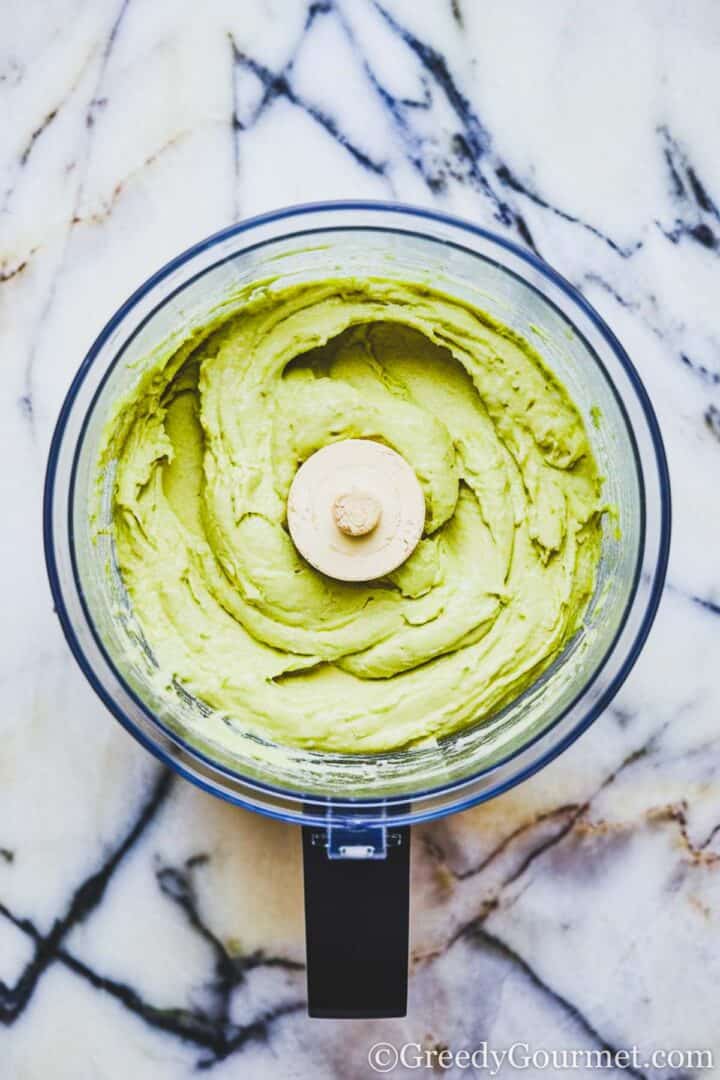 A smooth, green dip inside a food processor bowl on top of a grey marble surface.