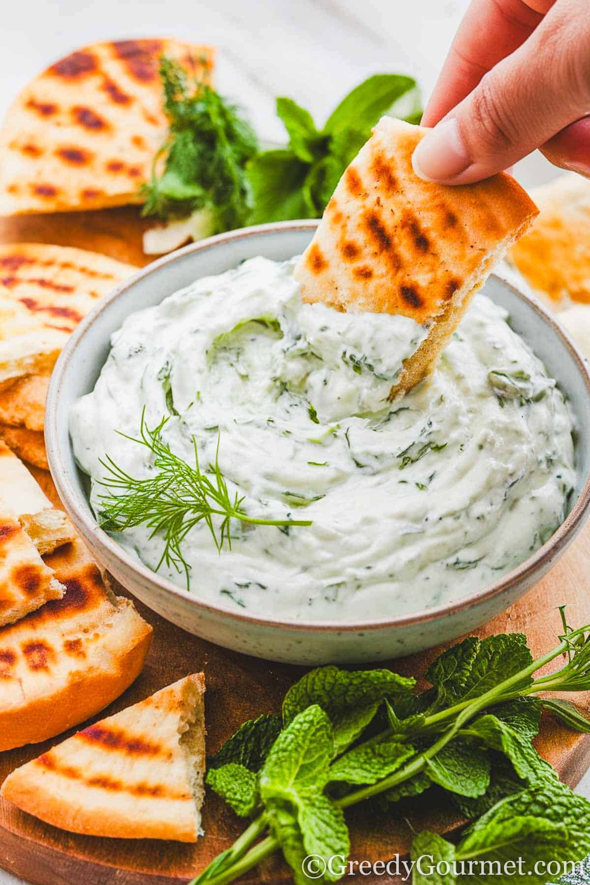 Bowl of tzatziki with hand dipping piece of bread in