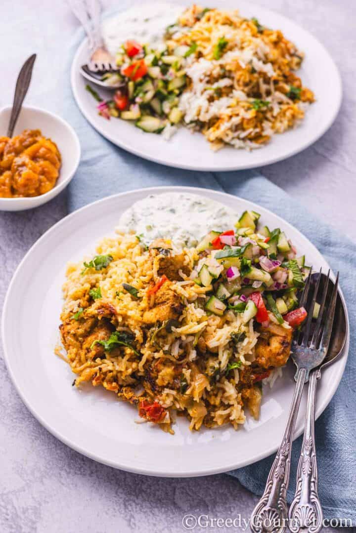 Chicken tikka biryani served on a white plate with a cucumber salad.