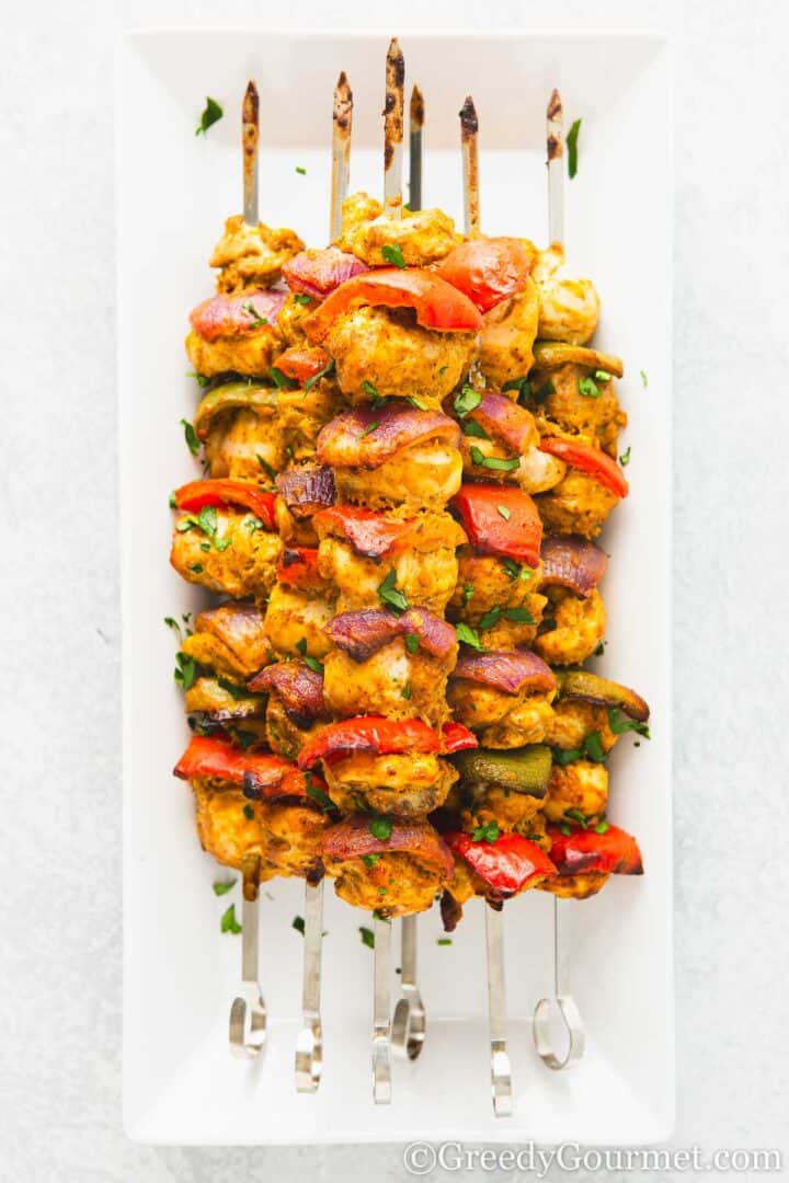 Chicken tikka skewers on a white plate.