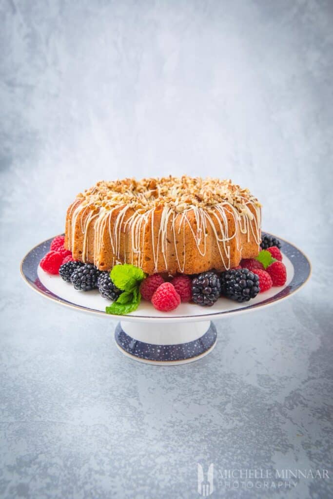 A brown bundt cake on a platter with berries underneath