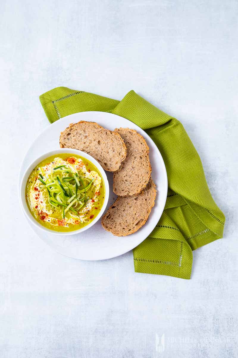 A bowl of zucchini and leek soup with three slices of brown bread and a green napkin