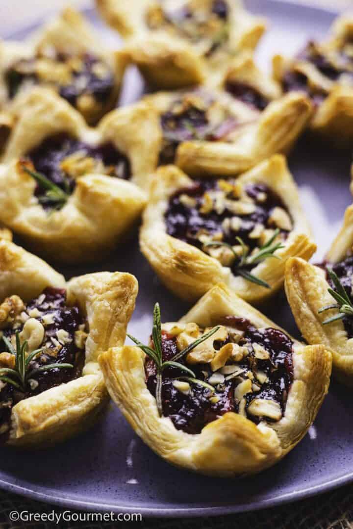 puff pastry cups filled with cheese and cranberry sauce, arranged on a blue plate with rosemary