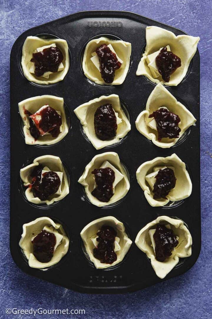 red jam in pastry cups in muffin tin on blue table top