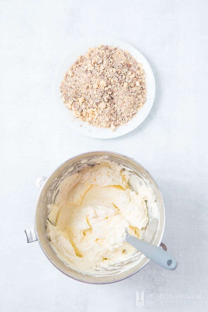 A bowl of cream cheese with crumbles of cookies on a plate to make a Maltesers cheesecake