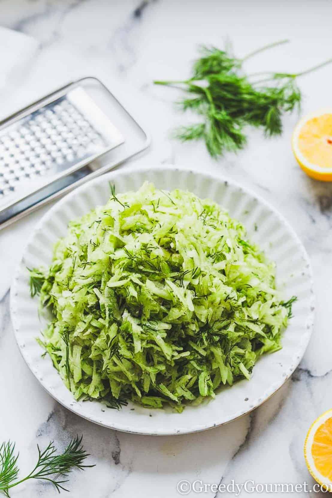 plate of grated cucumber with grater, lemon and dill on the side