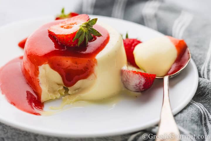 White Chocolate Panna Cotta served on a plate with strawberry halves.