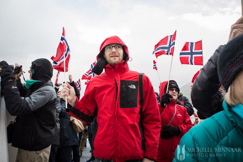 A man wearing a red jacket holding a Norweigen flag