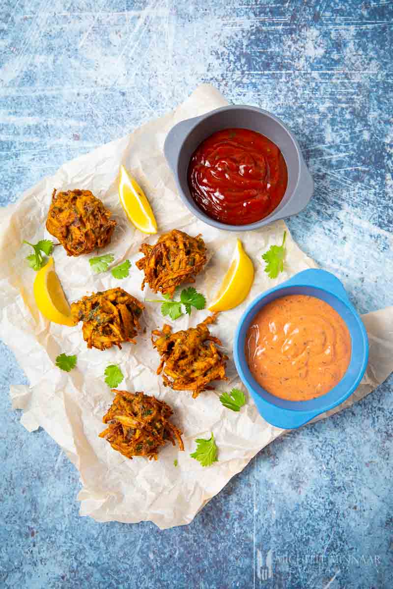 Balls of fried mushroom pakora and bowls of red and orange pakora sauce 