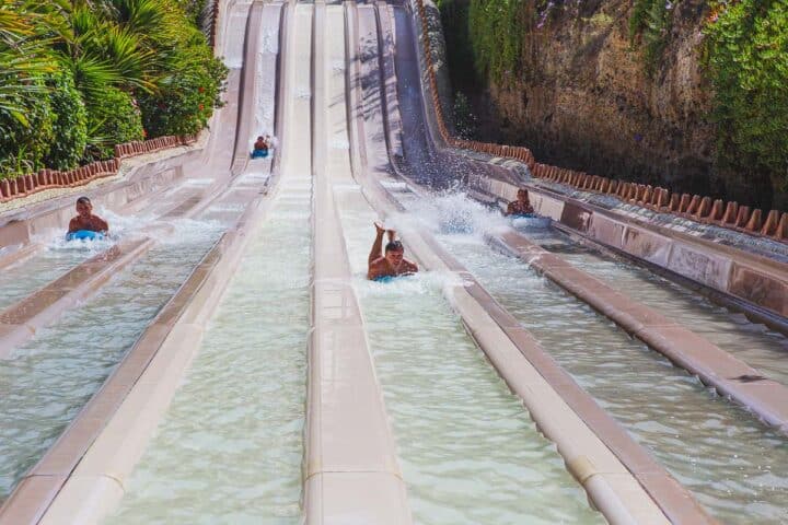 Four people riding separately on floats down a steep slope and making big splashes.