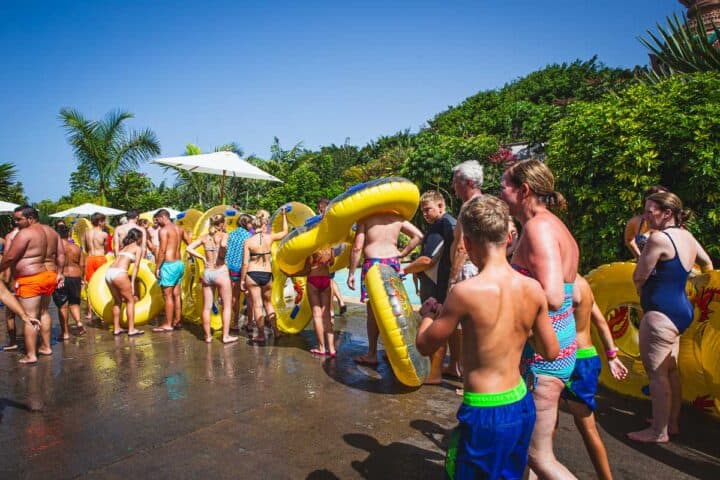 A massive queue of people holding yellow tubes while waiting for their rides in a lush green setting and pure blue skies.