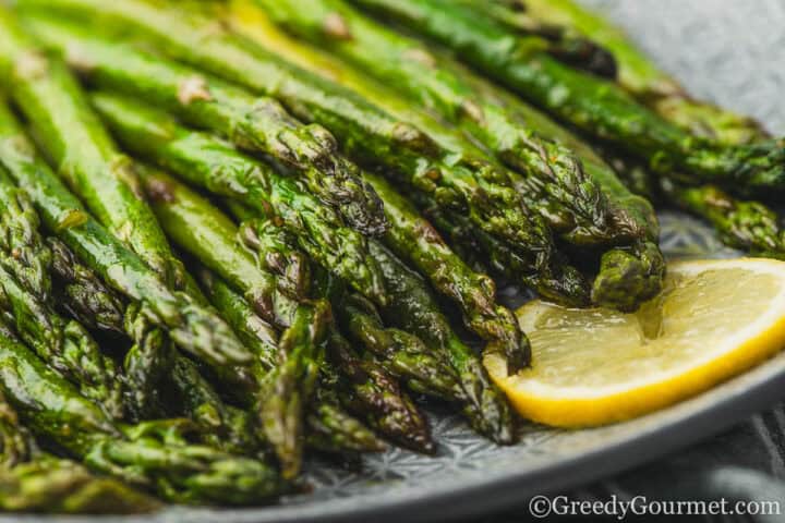 Roasted asparagus on a plate served with lemon slices.