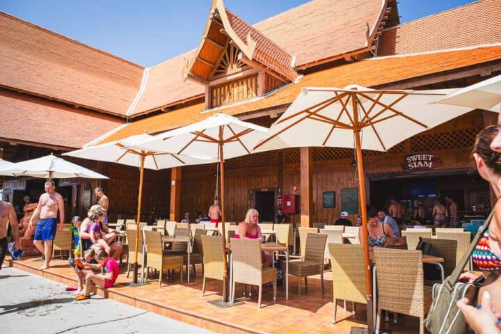 Sweet Siam is a restaurant in Siam Park selling all kinds of sweet goods. People are sitting underneath parasols at tables eating and resting. 