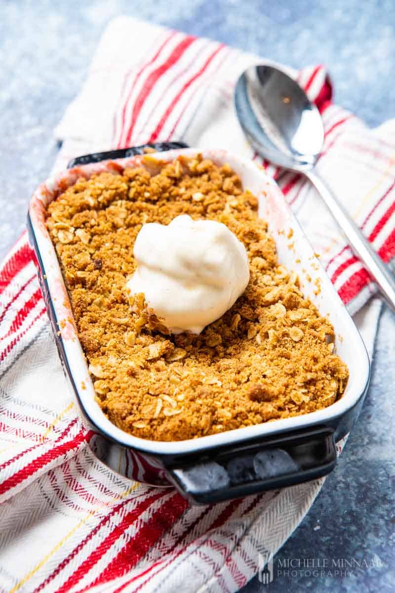 A apple and rhubarb crumble with a white scoop of ice cream 