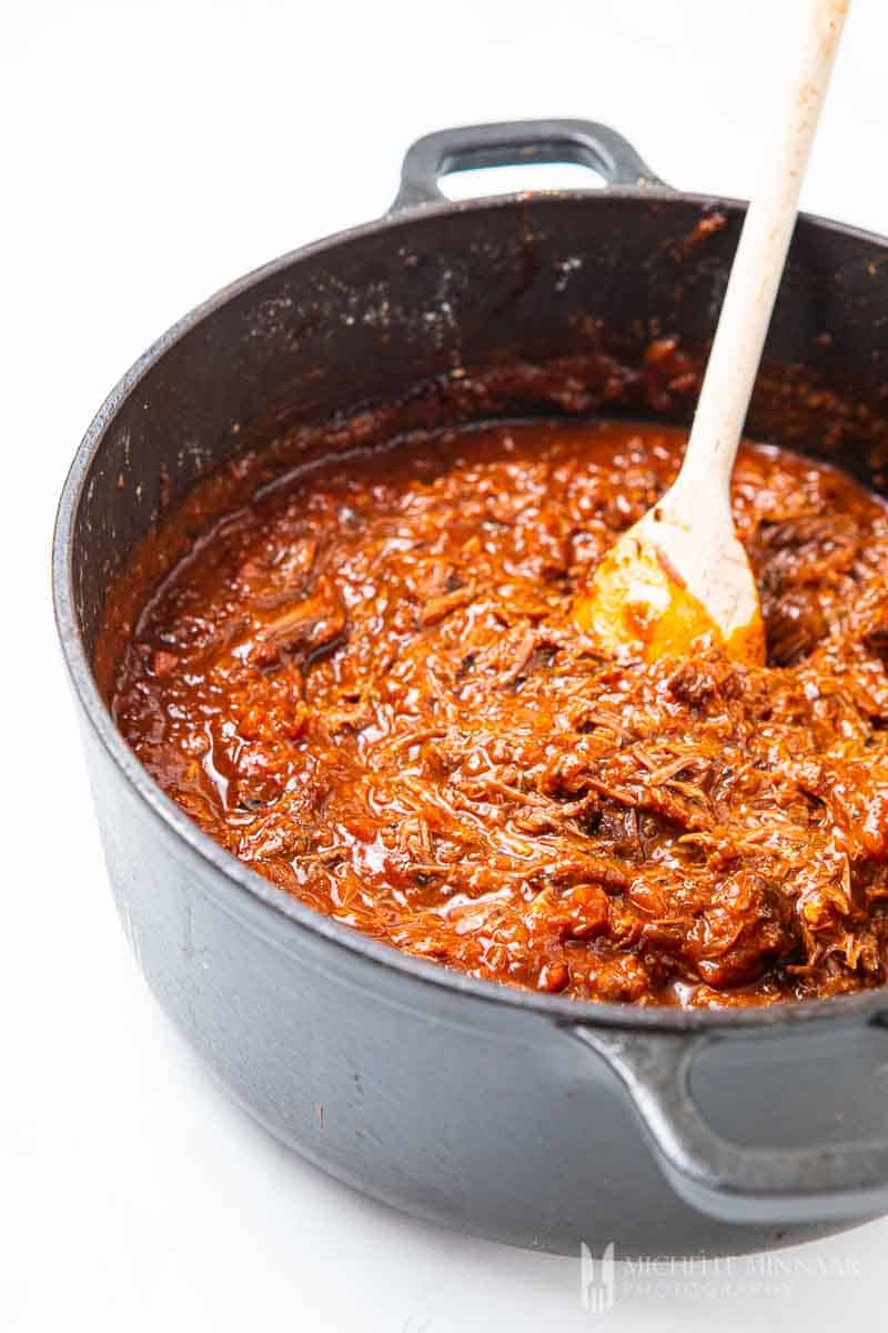 Beef simmering in a pot with red sauce