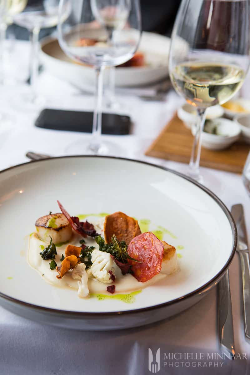 A close up of roasted veggies and scallop on a plate and wine 