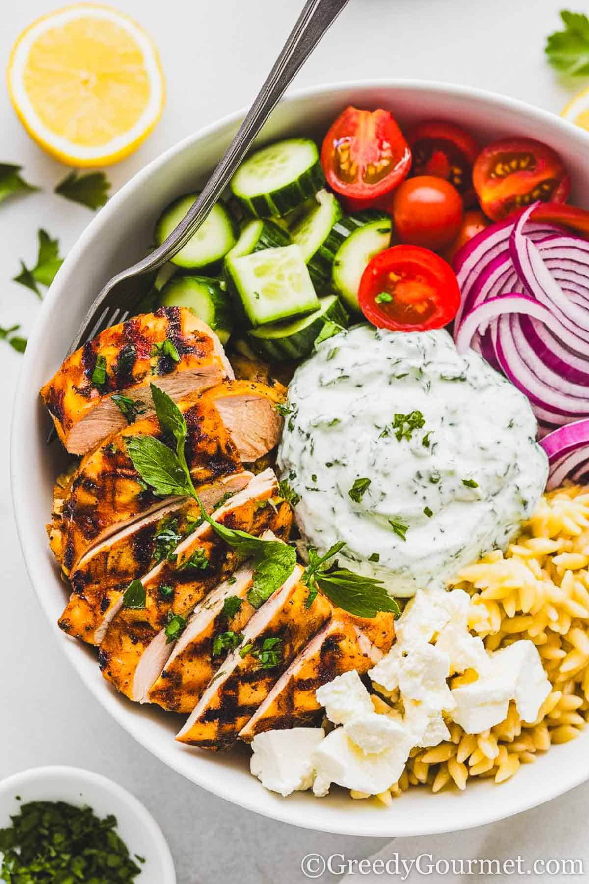 healthy chicken bowl with red onions, tomatoes, cucumbers, orzo, feta cheese and tzatziki