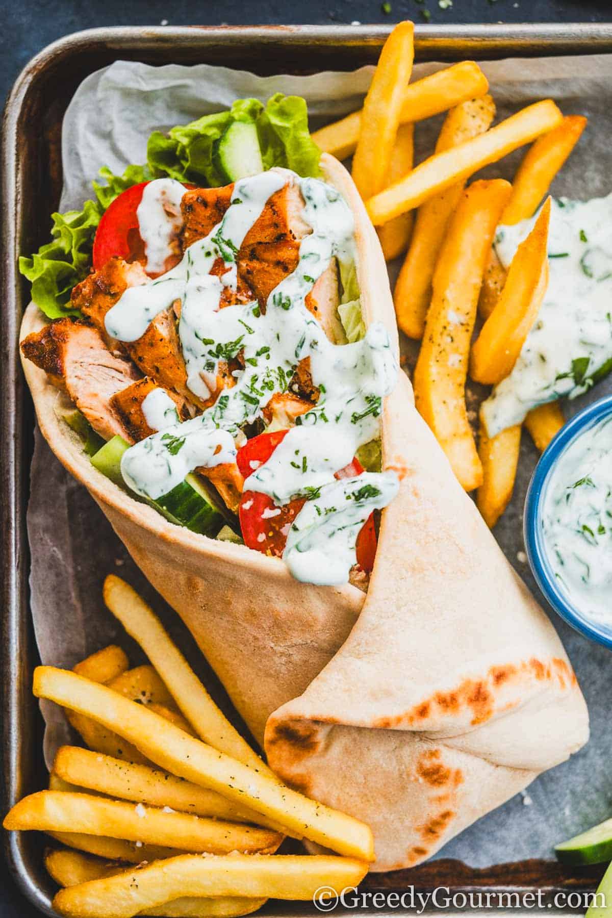 chicken gyros, sliced tomato and cucumber with lettuce, topped with tzatziki, wrapped in flatbread, surrounded by fries