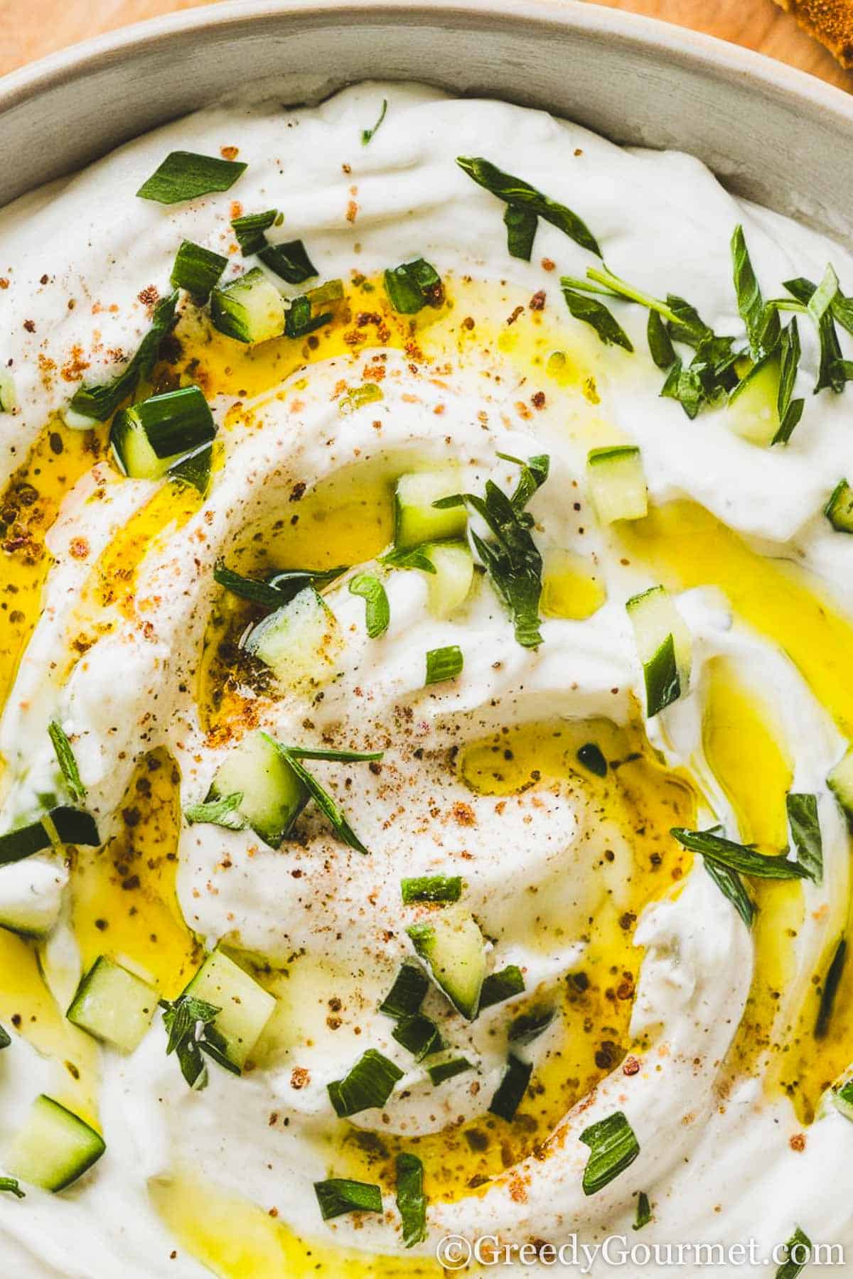 closeup of creamy tzatziki topped with finely chopped cucumber, mint, olive oil and dried chilli flakes