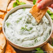 a person dipping a cracker into a bowl of creamy dip