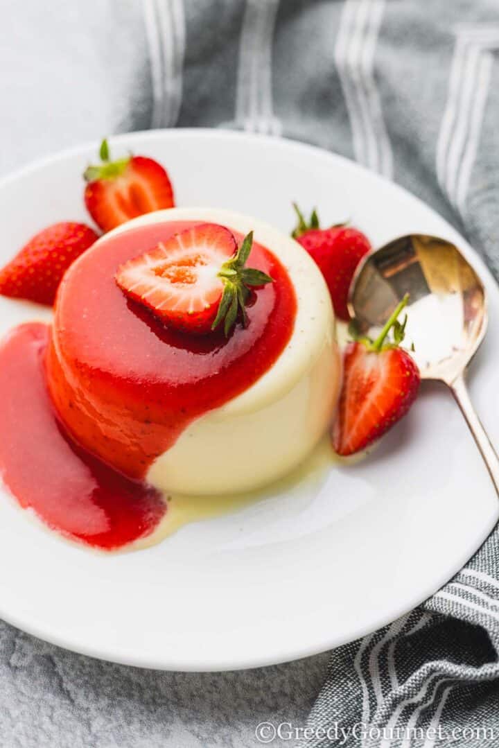 White Chocolate Panna Cotta served on a plate with strawberry halves.