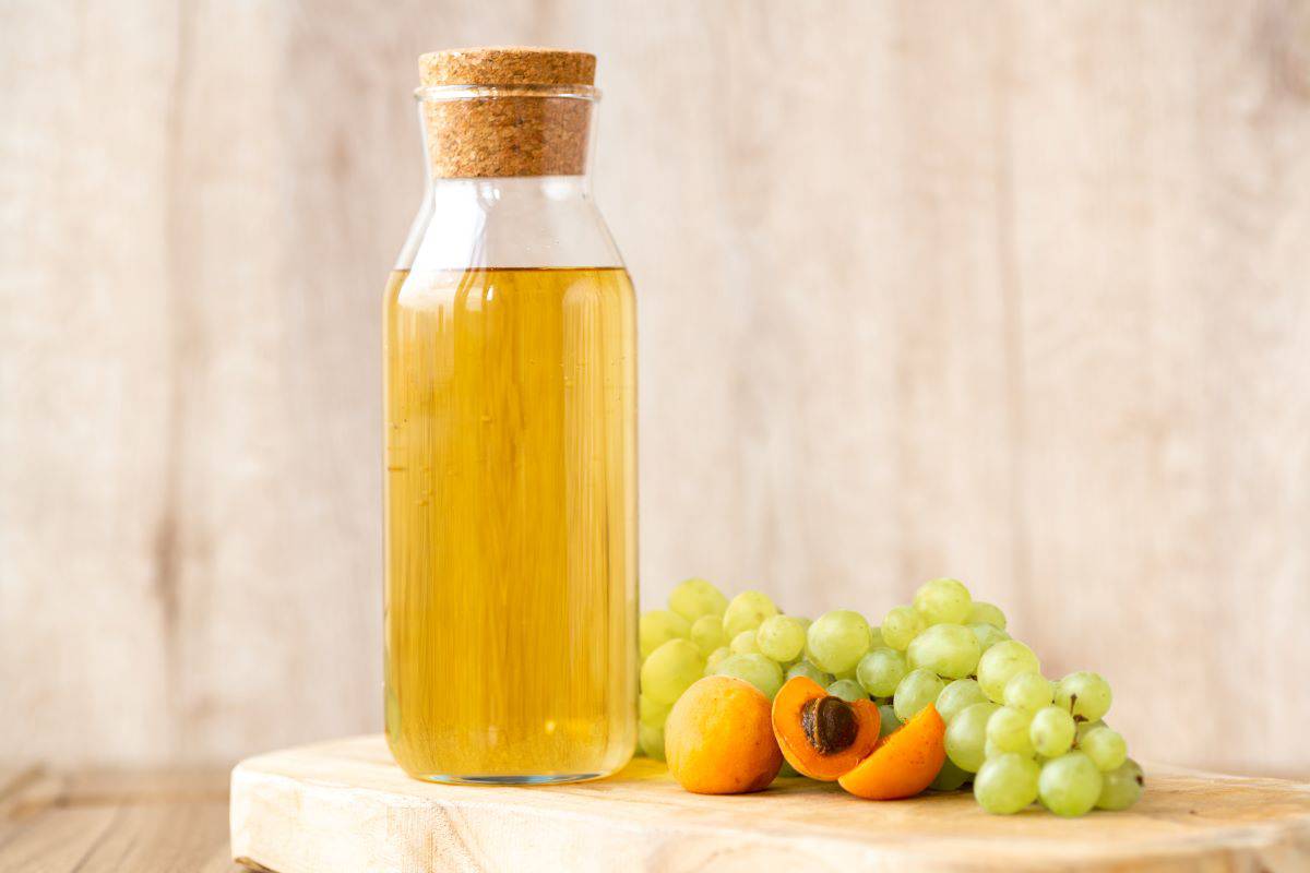 Glass bottle of white wine vinegar with a bunch of grapes next to it.