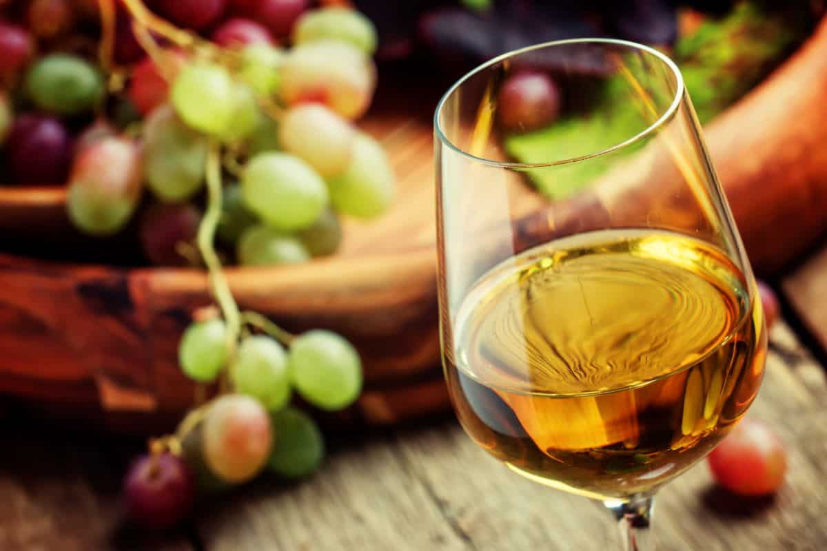 glass of white wine with grapes behind.