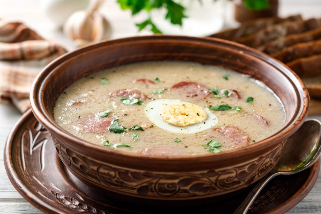 Zurek soup with a hard boiled egg served in a brown bowl.